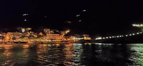 Illuminated city by sea against sky at night