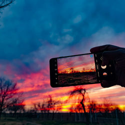 Person hand holding illuminated lighting equipment against sky at sunset