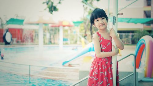 Portrait of smiling cute standing against swimming pool at water park