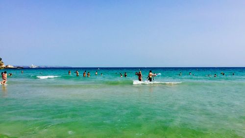 People on beach against clear blue sky