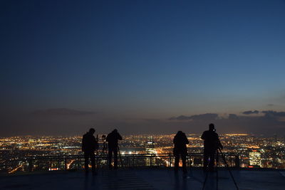 Silhouette people on terrace overlooking illuminated cityscape at dusk