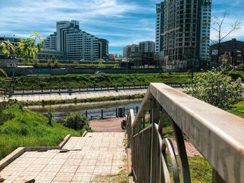 Footpath by buildings in city against sky