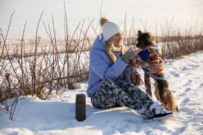 Full length of woman sitting on snow covered field