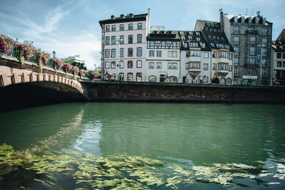 Bridge over river by buildings against sky