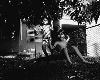 Portrait of shirtless brothers swinging in yard