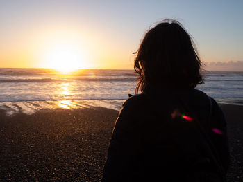 Rear view of woman looking at sea during sunset