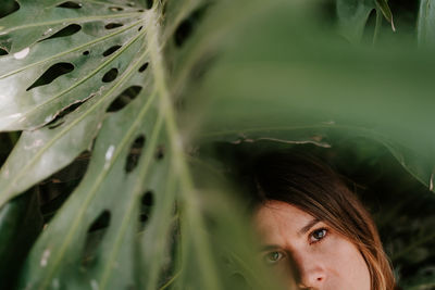 Young serene female standing in tropical park with monstera plants and looking at camera