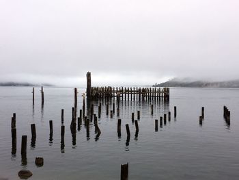 Wooden posts in lake against sky