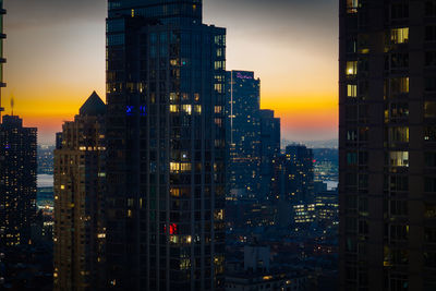 Illuminated buildings in city against sky during sunset