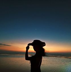 Silhouette woman standing at beach during sunset