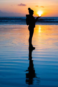 Sunset silhouette holding the sun on the beach.