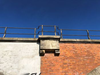 Low angle view of brick wall against clear blue sky