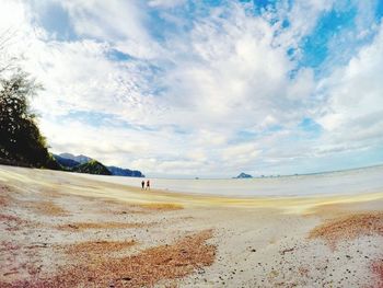 Friends running at beach against cloudy sky