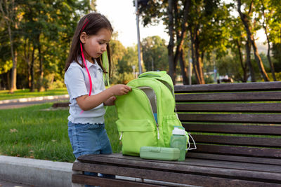 Child exploring backpack in park on sunny day