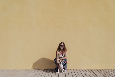 Portrait of smiling young woman sitting against wall