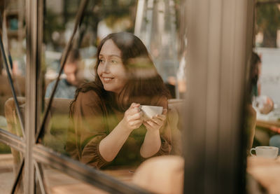 Portrait of woman holding coffee cup by window