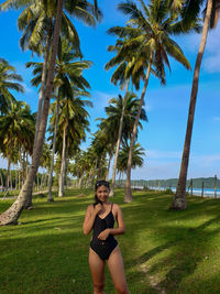 Portrait of young woman on palm trees on field against sky