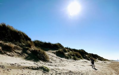 Man walking at beach against clear sky during sunny day