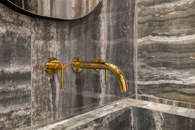 Close-up on modern golden tap in bathroom washbasin with marble wall tiles