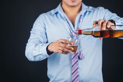 Midsection of man holding drink against black background
