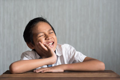 Portrait of smiling boy with eyes closed sitting at desk in classroom