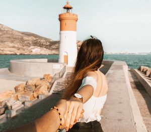 Cropped image of boyfriend holding girlfriend hand against lighthouse