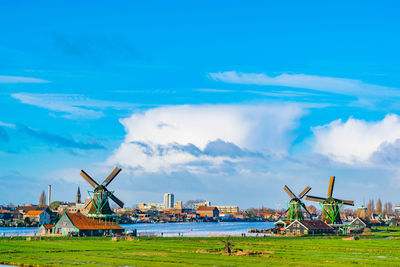Traditional windmills on field by lake against blue sky
