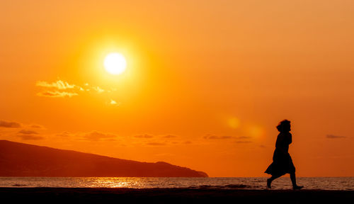 Woman running at beach, watching the sunset, silhouette.