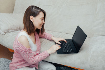 Young woman using online communities while sitting on sofa at home