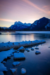 Scenic view of lake by snowcapped mountains against sky during sunset