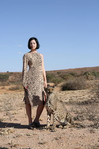Portrait of woman with cheetah standing on landscape against clear blue sky
