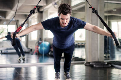 Sportsman doing exercise with fitness straps to strengthen his abdominal muscle in gym.