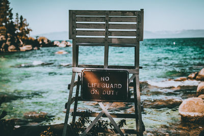 Lifeguard chair with warning message at beach against sky