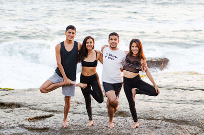 Full length portrait of smiling friends doing yoga at beach