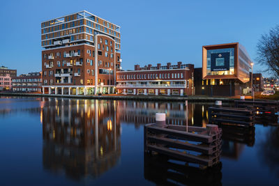 Reflection of buildings in river against clear sky