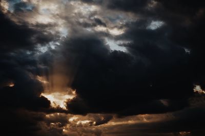 Low angle view of sunlight streaming through storm clouds