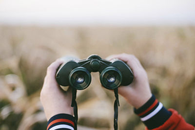 Cropped hands of woman holding binoculars at farm