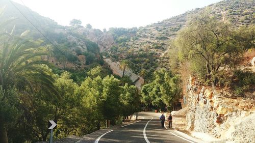 Woman walking on road amidst trees against mountains