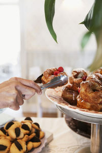 Cropped image of hand holding dessert with tongs by cakestand at cafe