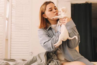 A cheerful young teenage woman plays with her pet a small dog in bed in the morning in a cozy house