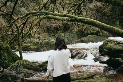 Rear view of woman looking at waterfall in forest