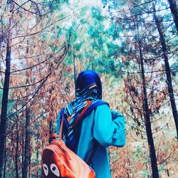 Rear view of man standing by trees in forest