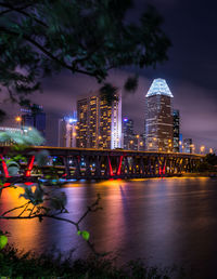 Illuminated buildings by river against sky in city at night