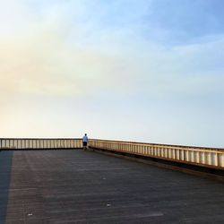 Man walking on footbridge over sea against clear sky