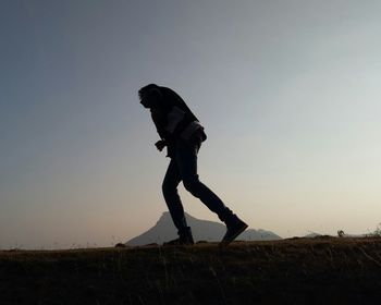 Full length of man walking on field against clear sky during sunset