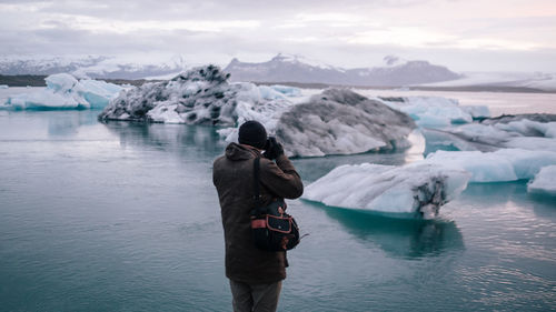 Man photographing with camera in winter against sky