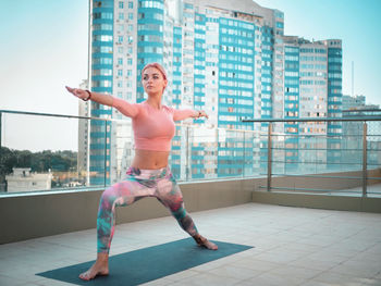 Full length of young woman exercising yoga on building terrace in city