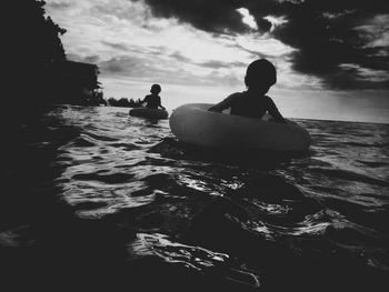 Silhouette children swimming with inflatable rings in sea