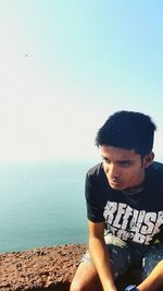 Young man sitting on retaining wall against sea