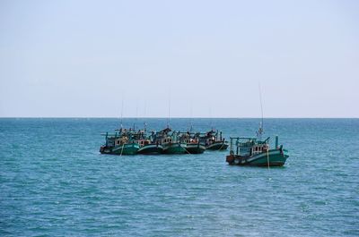 Boats sailing in sea against clear sky on sunny day